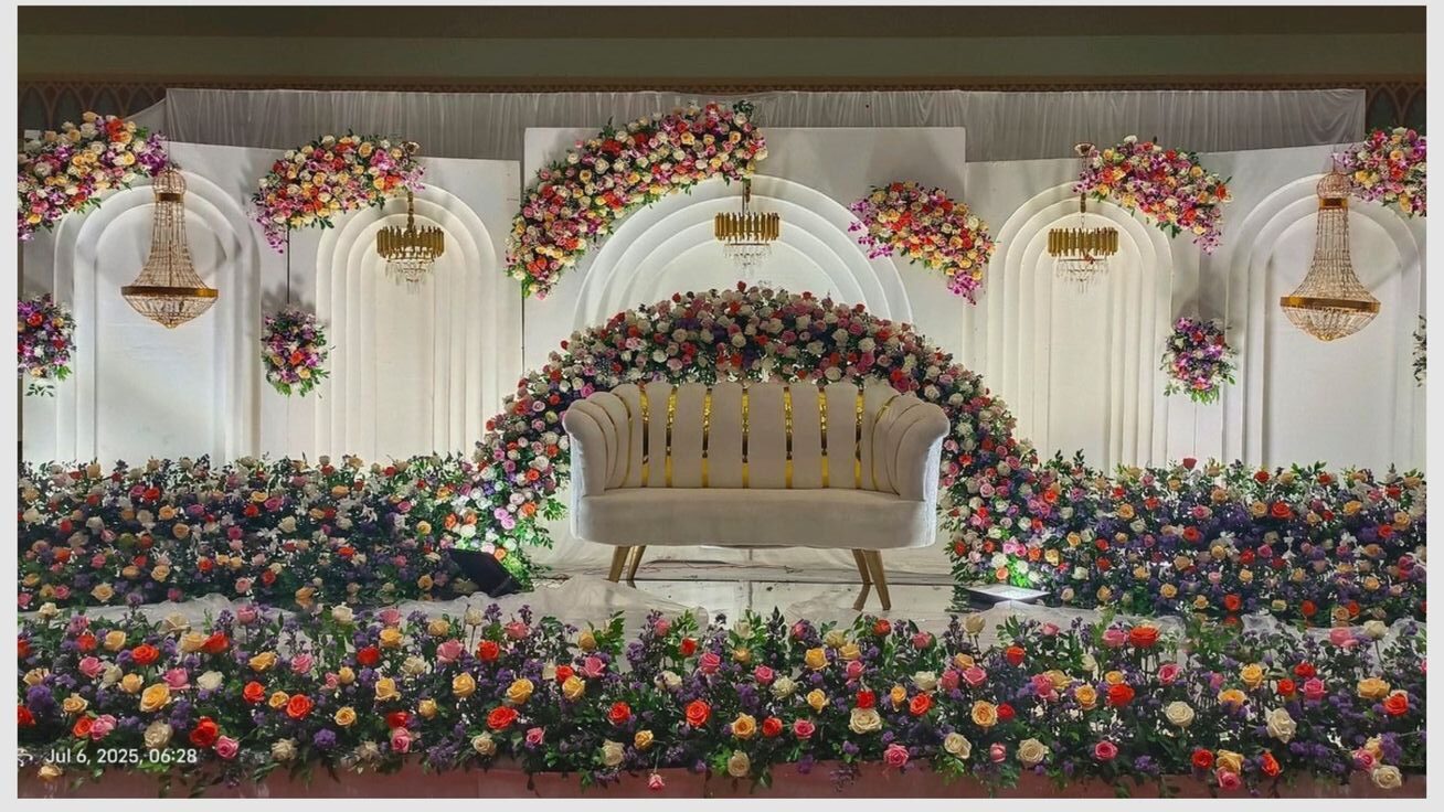 Elegant engagement stage decoration with white luxury backdrop, chandeliers, pastel floral arch, and modern sofa setup in Hyderabad.