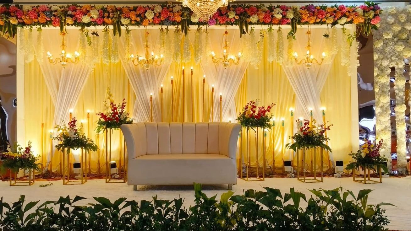 Luxury reception stage decoration with warm candlelight theme, chandeliers, floral top styling, and elegant sofa setup in Hyderabad.