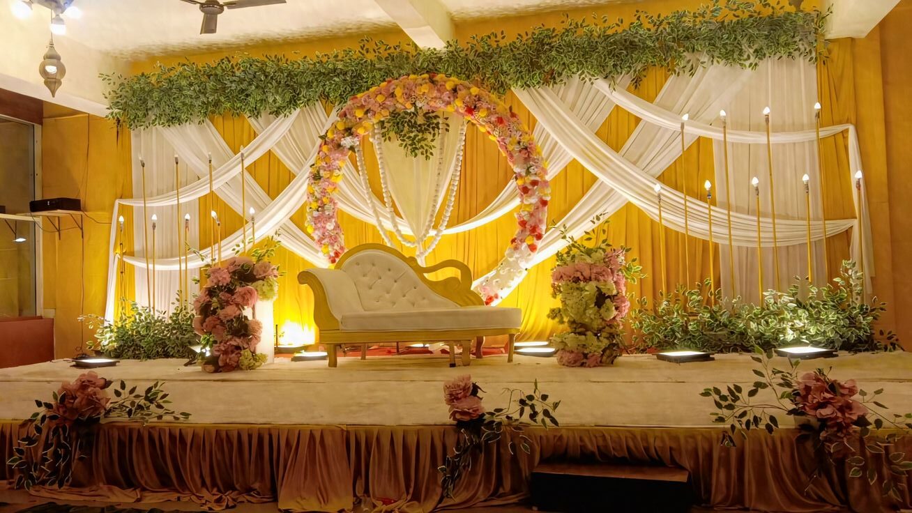 Luxury reception stage decoration with warm candlelight theme, chandeliers, floral top styling, and elegant sofa setup in Hyderabad.