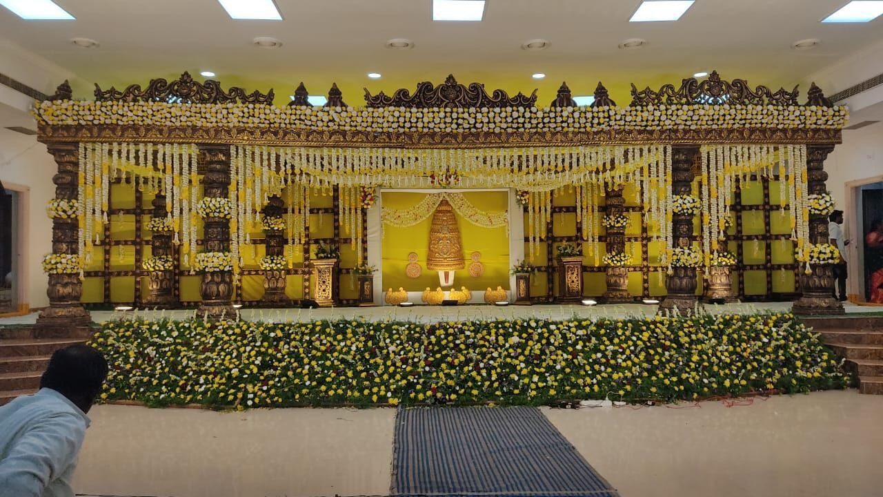 Beautiful traditional yellow floral wedding stage decoration with temple-style carved backdrop for South Indian weddings in Hyderabad.
